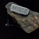 Srebrny prostokątny naszyjnik z ażurowym roślinnym wzorem, leżący na kamieniu