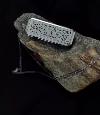 Srebrny prostokątny naszyjnik z ażurowym roślinnym wzorem, leżący na kamieniu