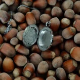 Srebrny otwierany naszyjnik z ażurową mandalą na tle orzechów laskowych.