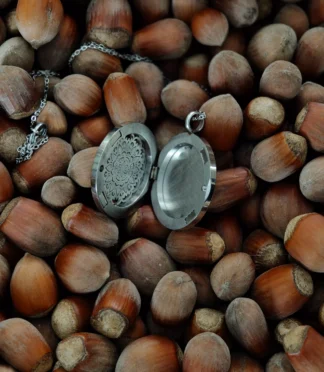 Srebrny otwierany naszyjnik z ażurową mandalą na tle orzechów laskowych.