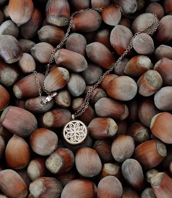 Naszyjnik z różowego złota z ażurowym wisiorem na tle orzechów laskowych