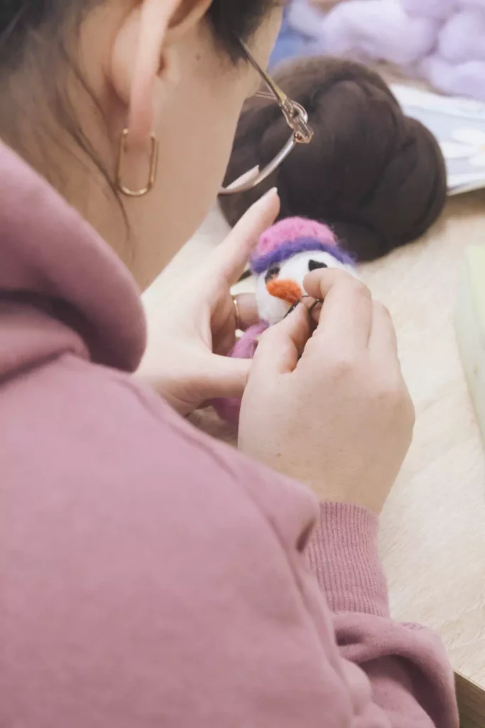 Ręce kobiety starannie formującej detale wełnianej zabawki podczas zajęć kreatywnych.