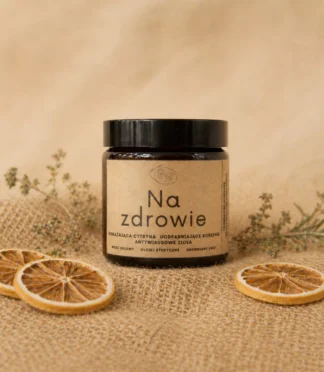 Świeca sojowa aromaterapeutyczna w szklanym słoiku z etykietą z napisem „Na zdrowie” wspierająca przy przeziębieniach/ Świeca sojowa w szklanym słoiku z etykietą z napisem "Na zdrowie" i dekoracjami w tle.