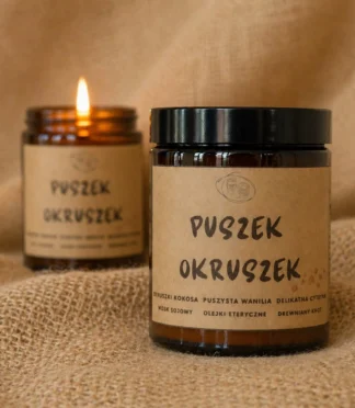 Dwie świece sojowe w szklanym, brązowym słoiku z etykietą z napisem "Puszek okruszek".